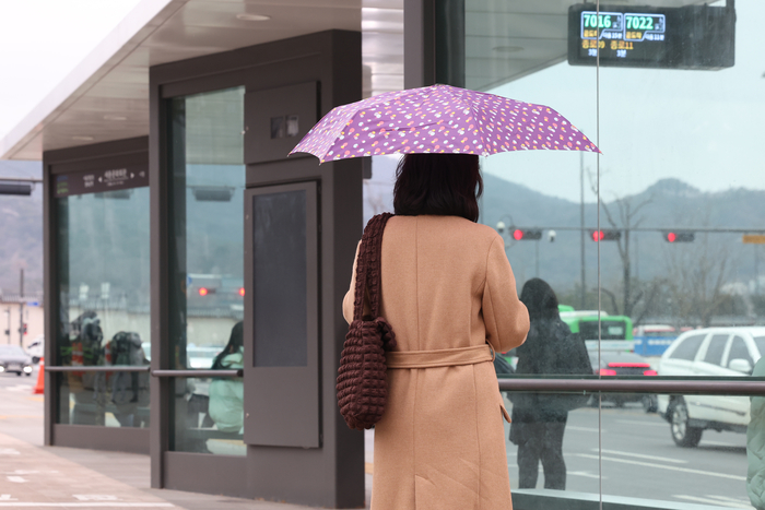 서울 종로구 광화문광장에서 한 시민이 우산을 쓰고 버스를 기다리고 있다.연합뉴스